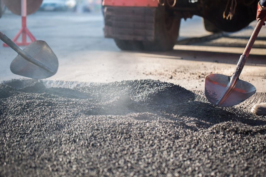 Workers shoveling asphalt on a road with a truck in the background.
