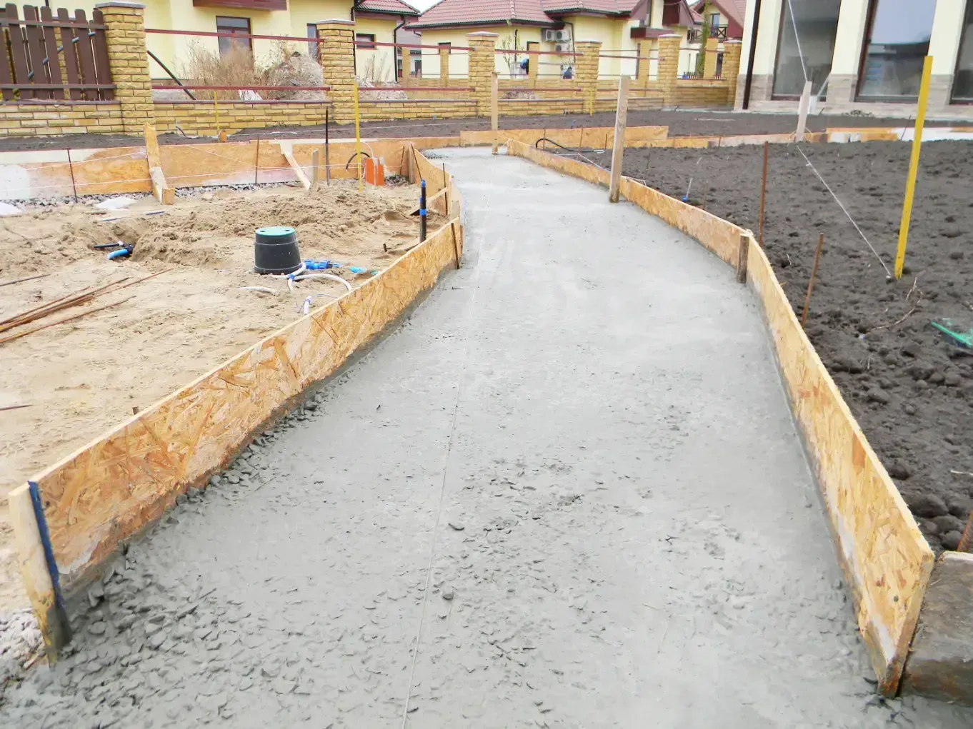 Freshly poured concrete walkway with wooden borders in a residential setting.