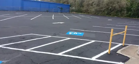 Parking lot with marked spaces; blue building in the background. Yellow railing on the right.