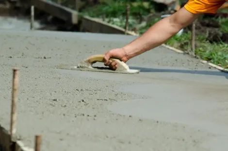 Person smoothing fresh concrete with a trowel. Outdoors, in progress.
