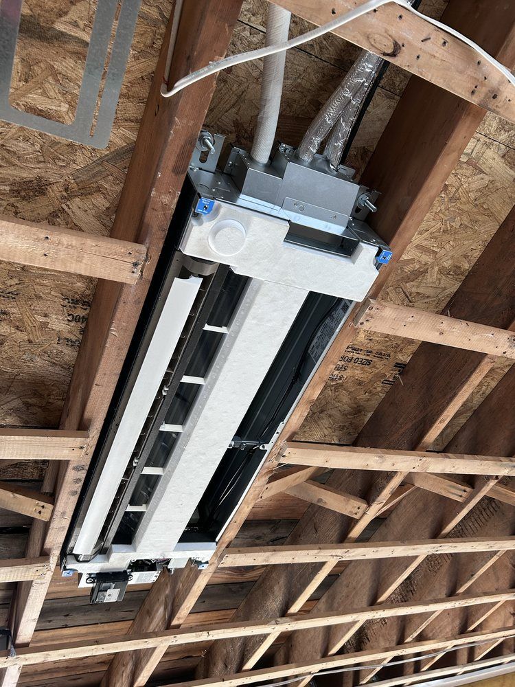 An air conditioning unit installed in a wooden ceiling, silver metal with exposed wiring.