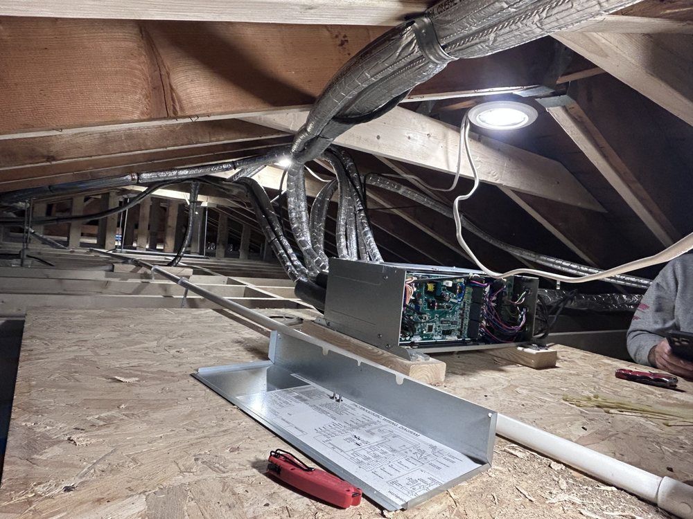 View of an attic with electrical wiring, an open server, and a work light illuminating the space.