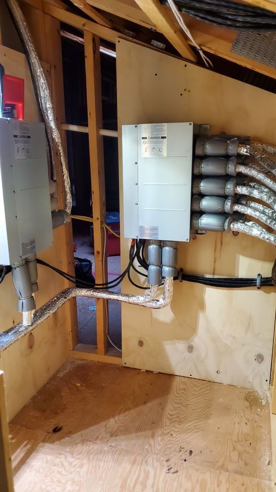 Solar panel in an attic space, showing wiring and ductwork. Wooden walls and beams are visible.