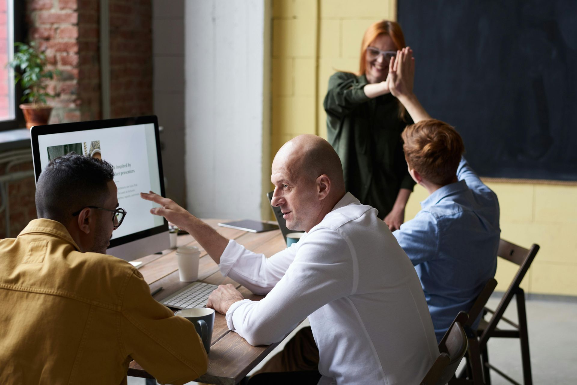 People collaborating around a computer screen. Woman giving high five to a man, while others discuss.