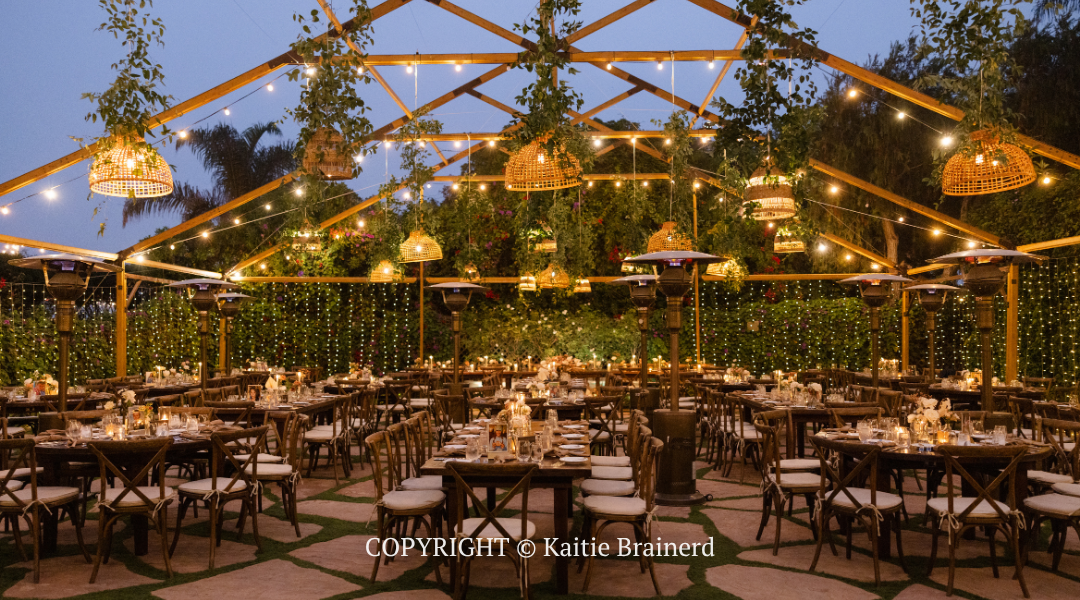 Elegant outdoor dining venue with string lights, wooden beams, and tables set amid lush greenery at dusk