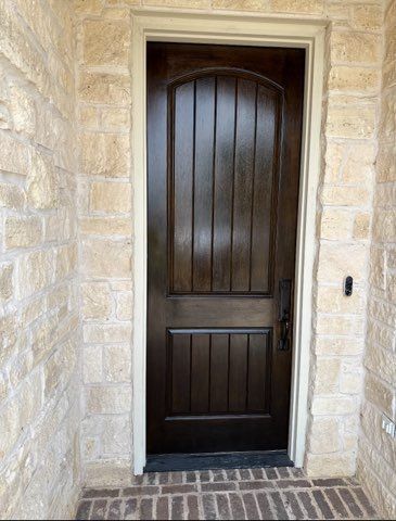 Wooden door, dark brown with vertical panels, set in beige stone entryway.