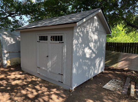 Gray shed with double doors, set in a yard with trees.
