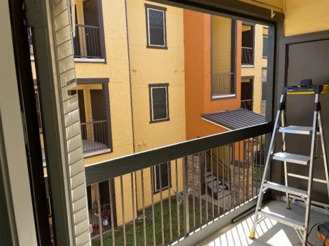 Balcony with retractable screen; view of apartment building. Silver ladder, tools, railings, and screen frame are visible.