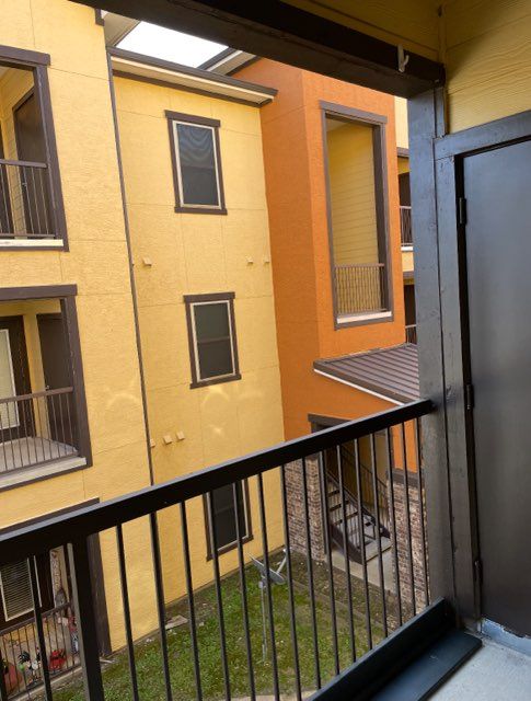 View from a balcony of yellow and orange apartment buildings with brown trim and a grassy courtyard below.