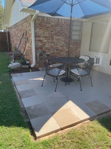 Patio with table, chairs, and umbrella next to a brick house, on a sunny day.