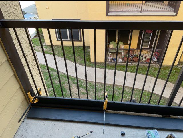 Black railing on a balcony with a wooden board clamped to the railing, view from above.