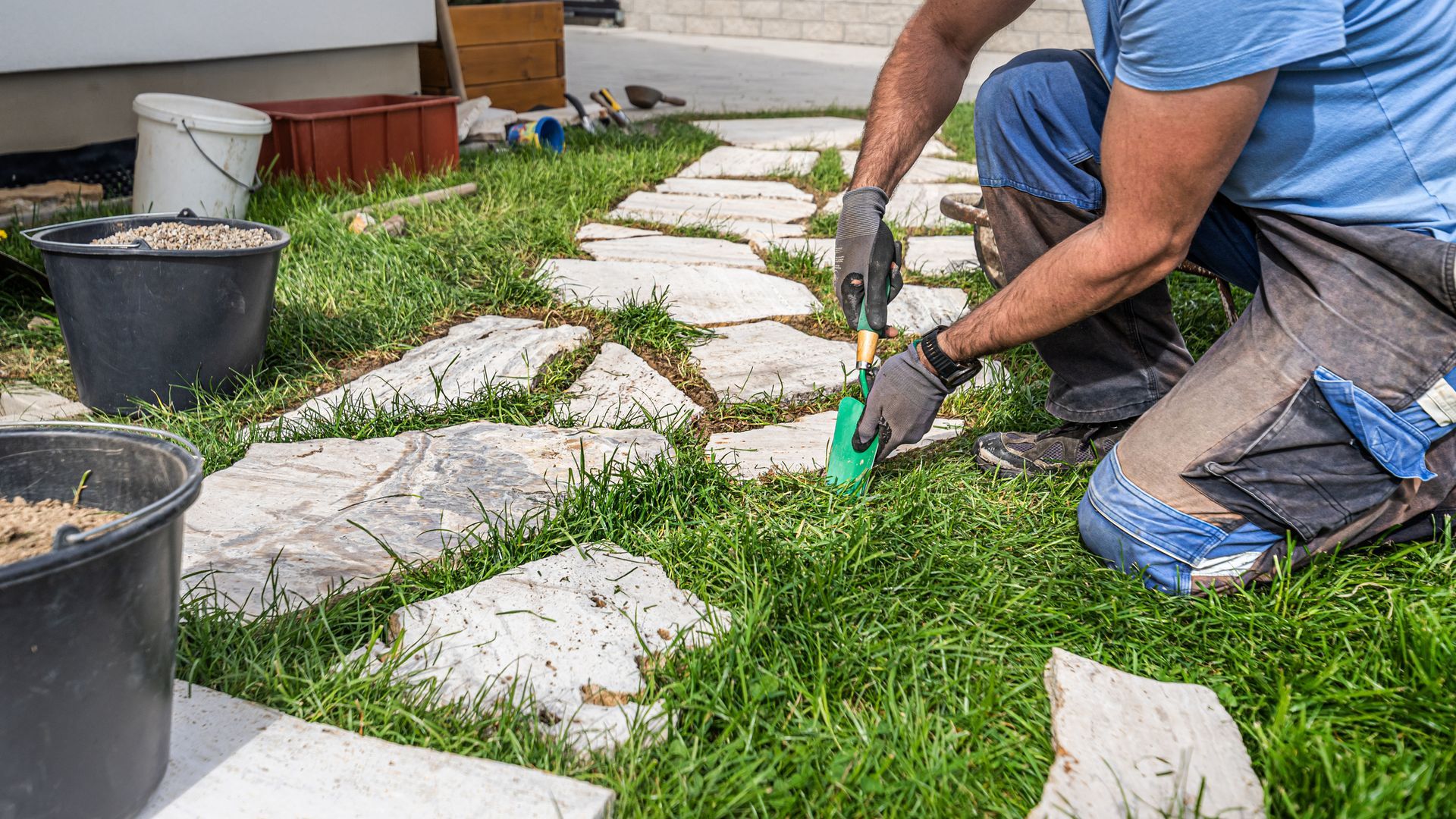 A man works on a stone path, illustrating skilled hardscaping services for outdoor landscaping.