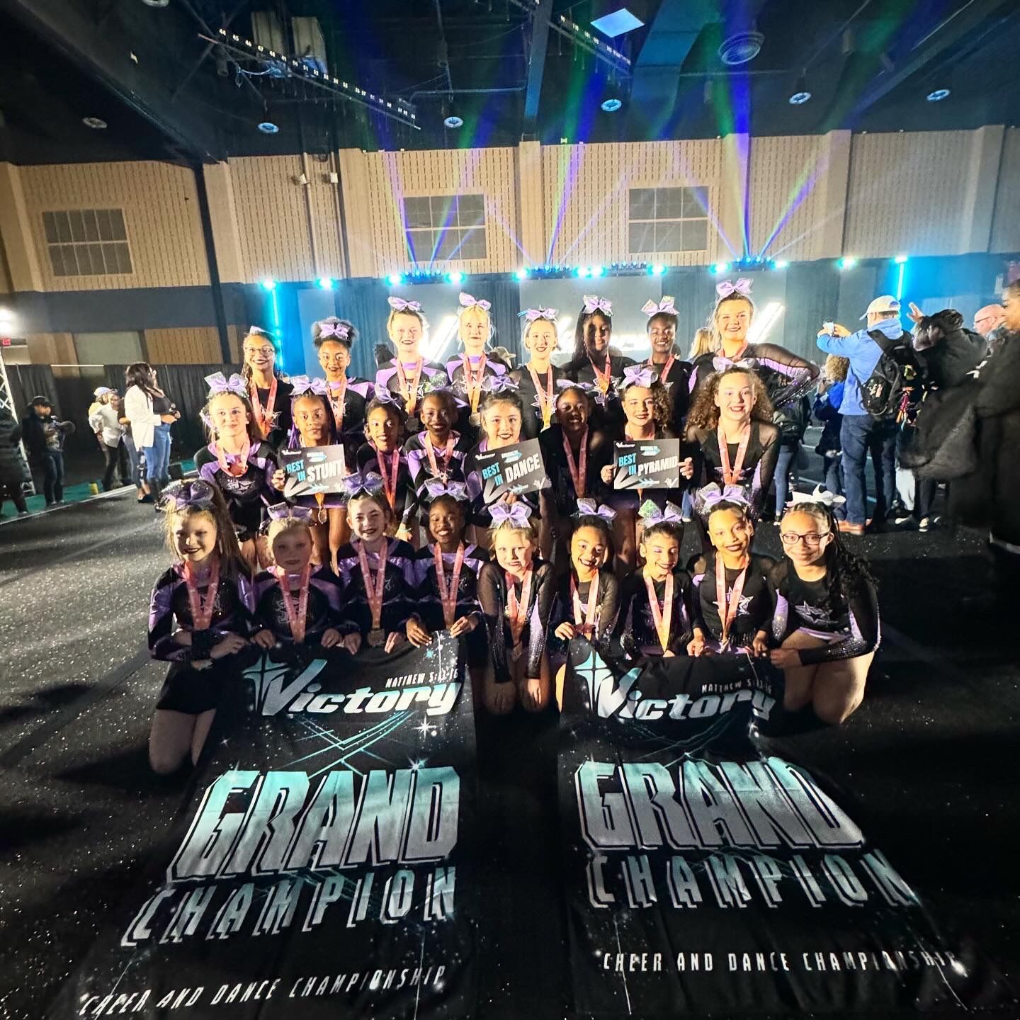 A group of cheerleaders are posing for a picture in front of a sign that says grand champion