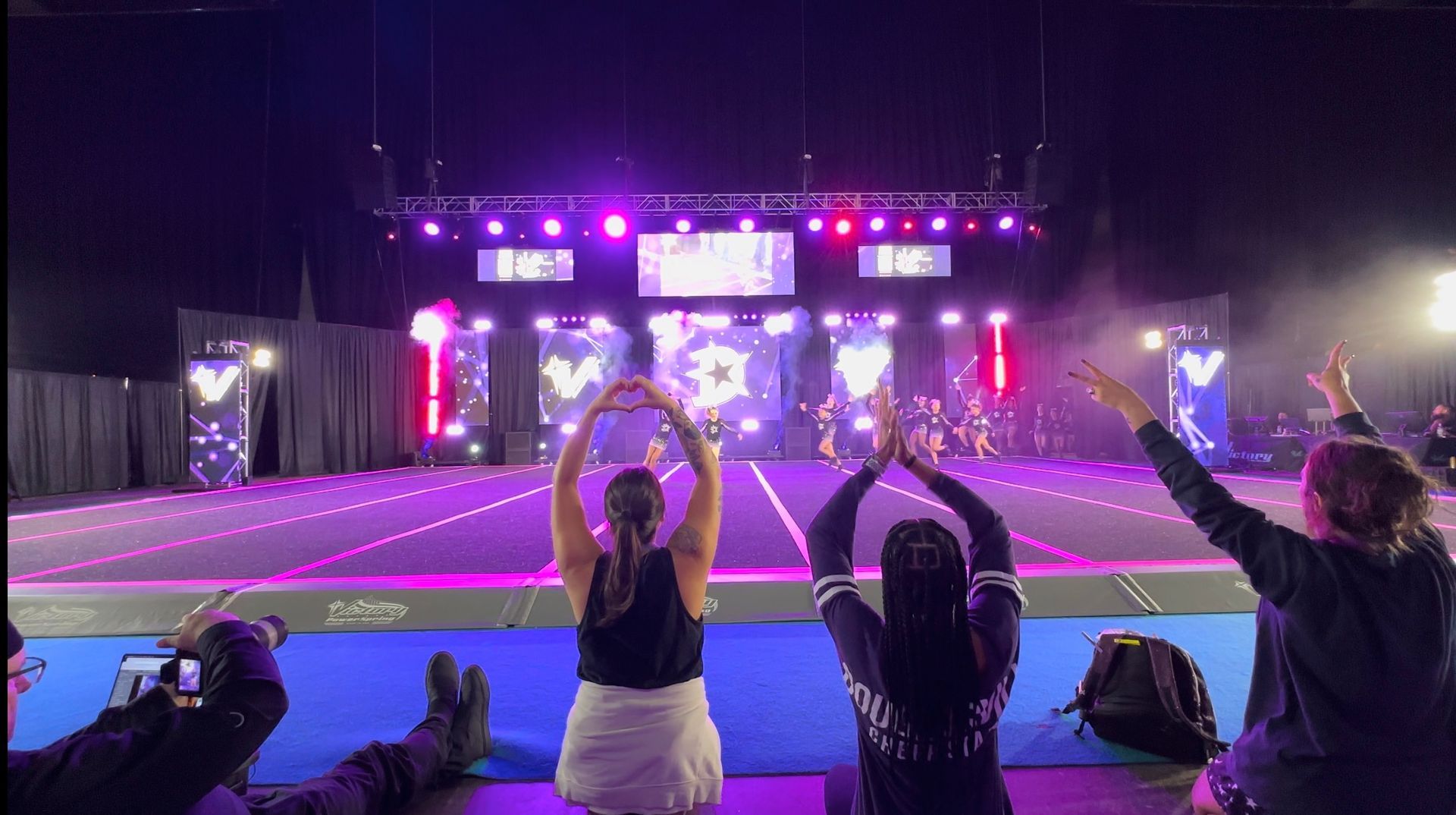 A group of cheerleaders are standing on a stage with their arms in the air.