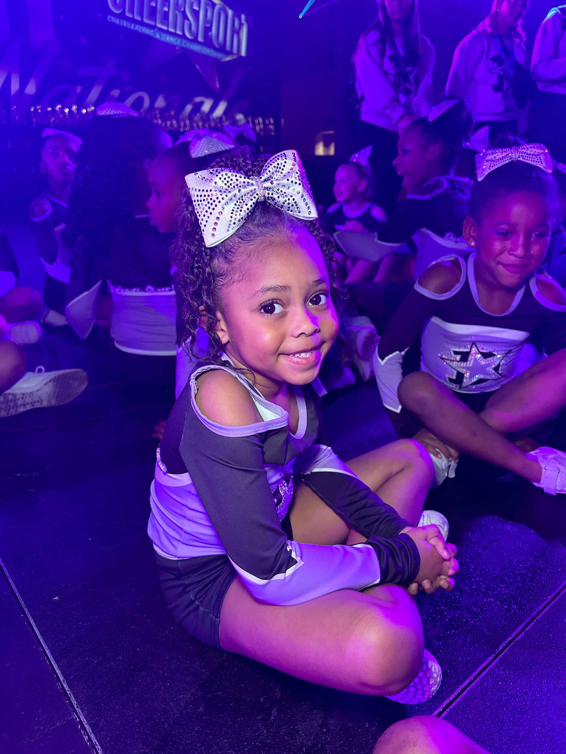 A little girl in a cheerleading uniform is sitting on the floor.