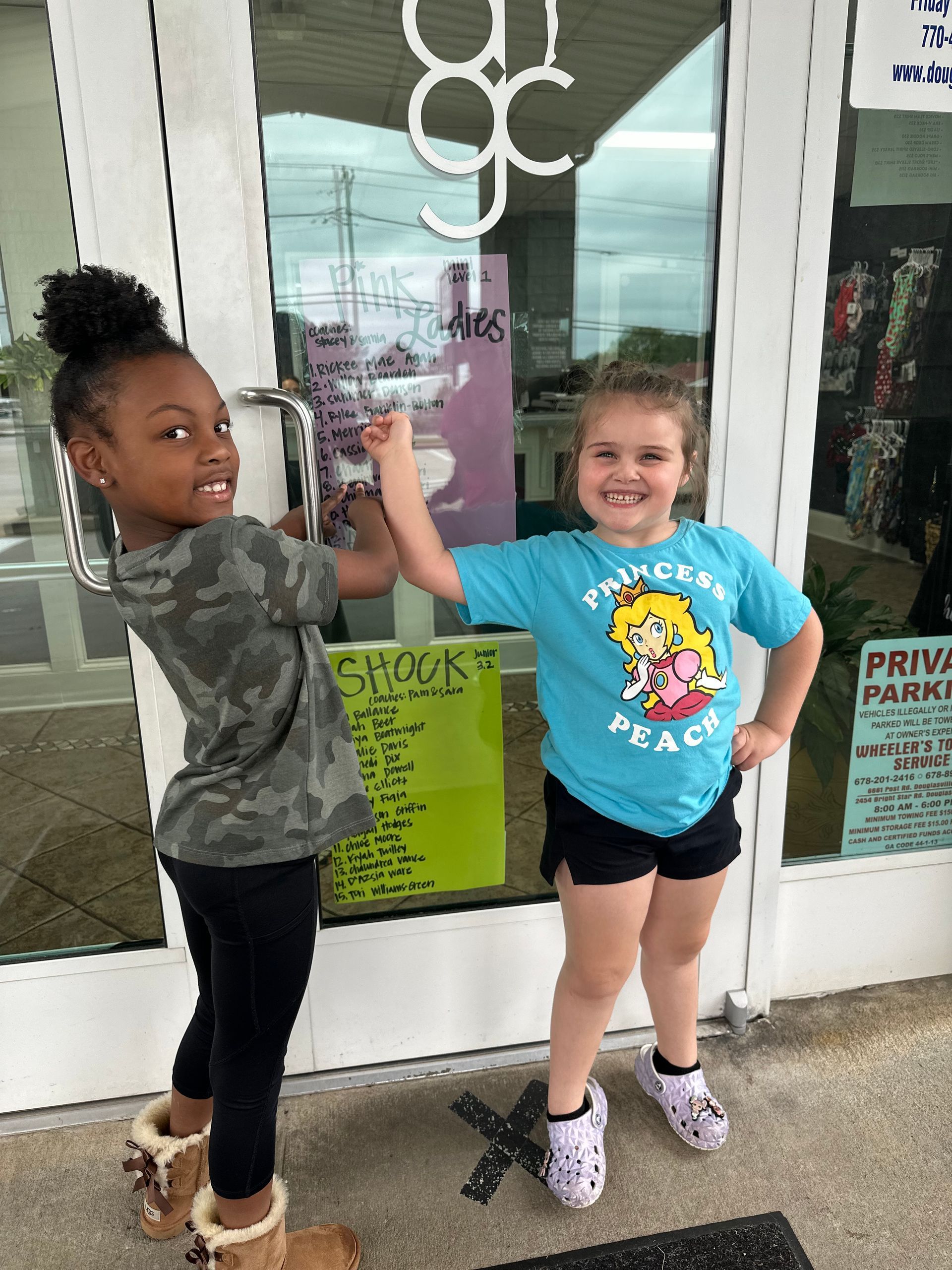 Two young girls are standing in front of a store door giving each other a high five.