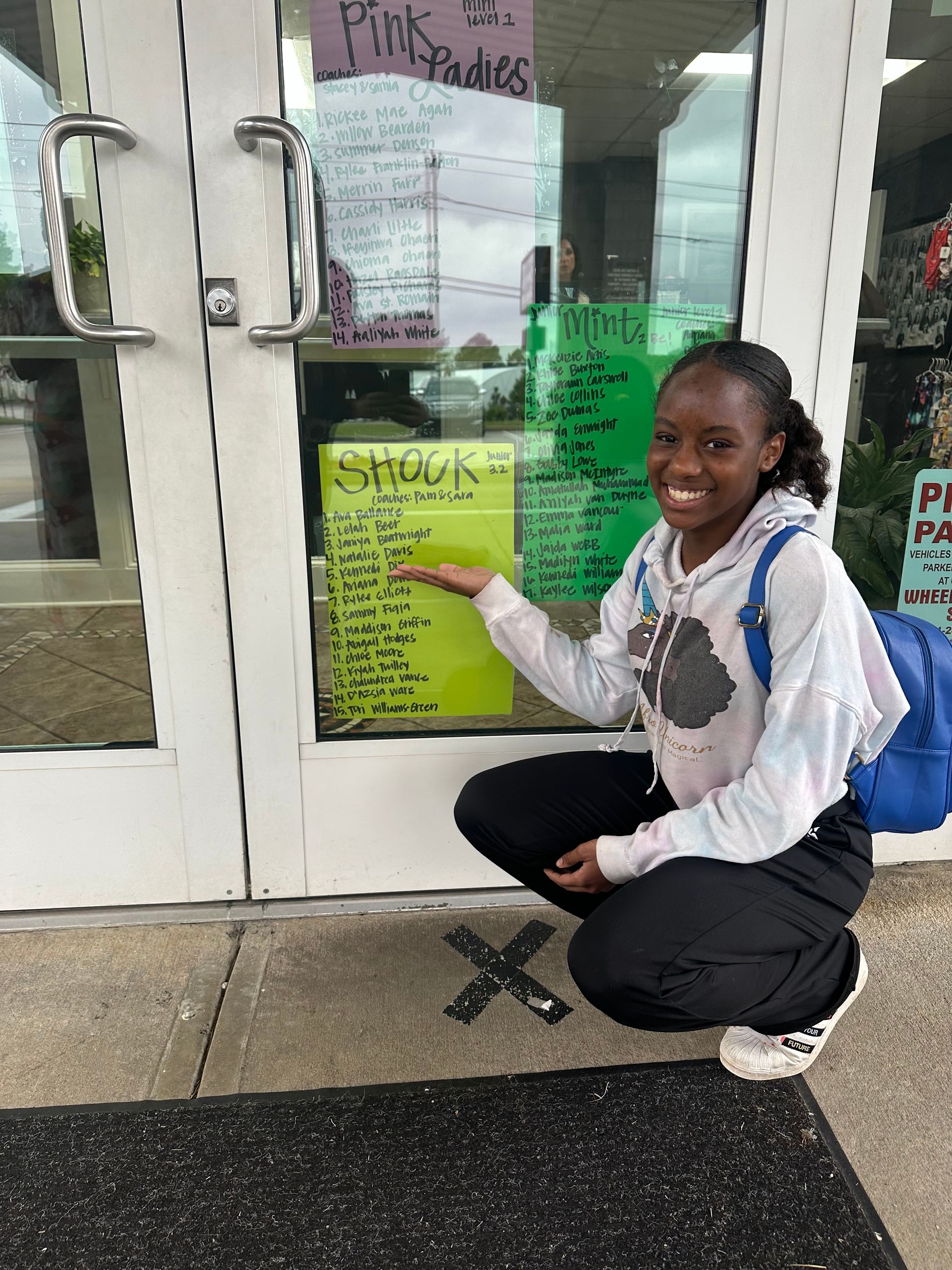 A girl is kneeling down in front of a door holding a yellow sign.