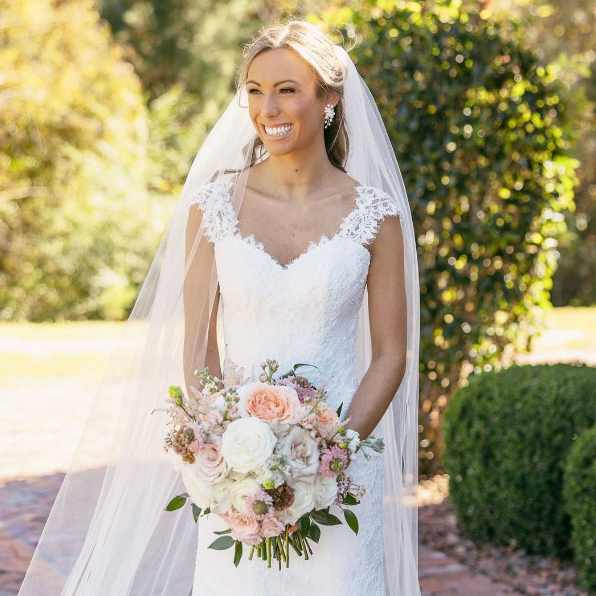 A bride in a wedding dress and veil is holding a bouquet of flowers.