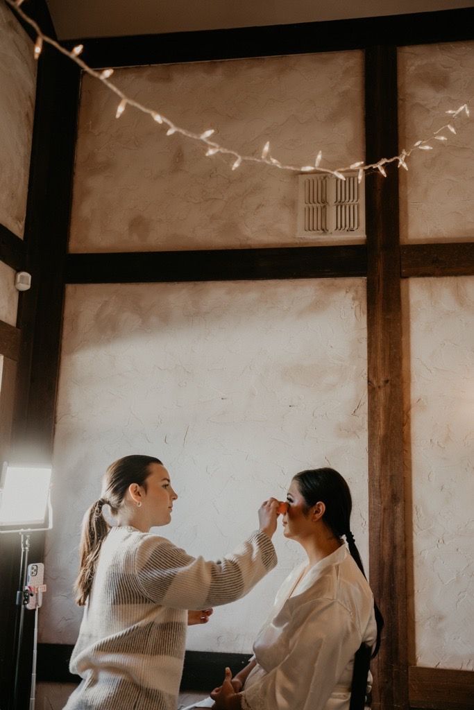 A woman is applying makeup to another woman in a room.
