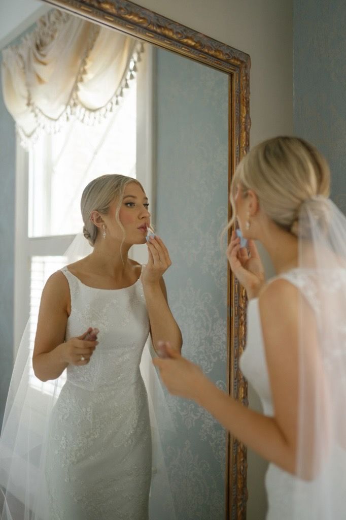 A bride is applying lipstick in front of a mirror.