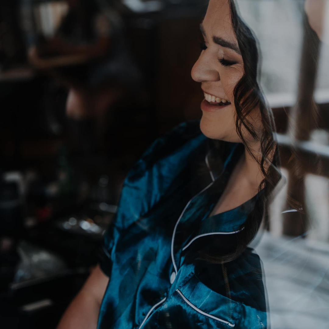 A woman in a blue shirt is smiling in front of a window.