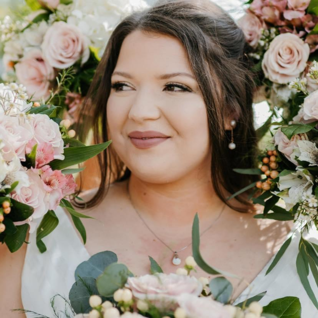 A woman in a white dress is holding a bouquet of pink flowers.