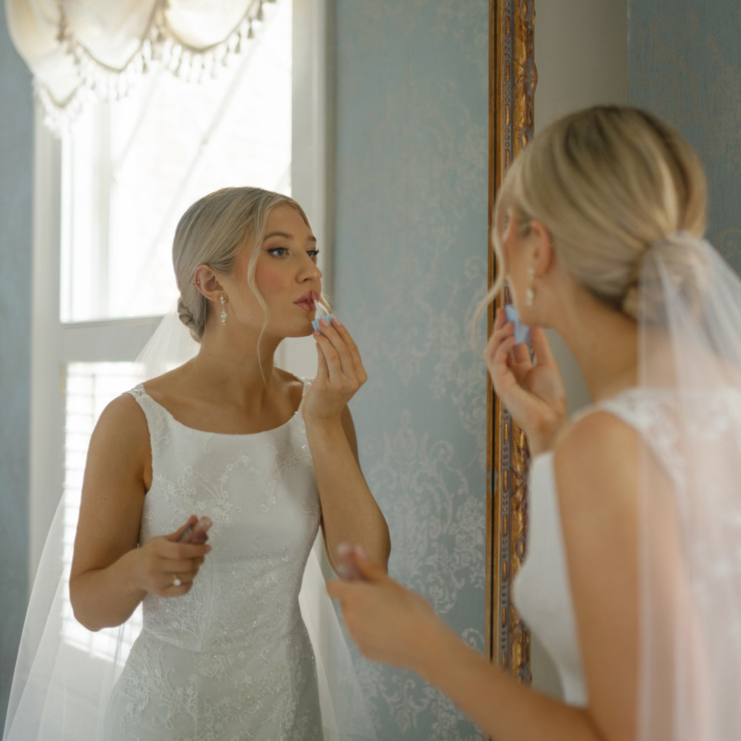 A bride is applying lipstick in front of a mirror.