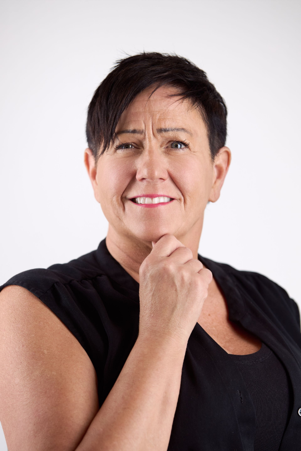 Woman with short dark hair, hand on chin, smiling, wearing black shirt against white background.