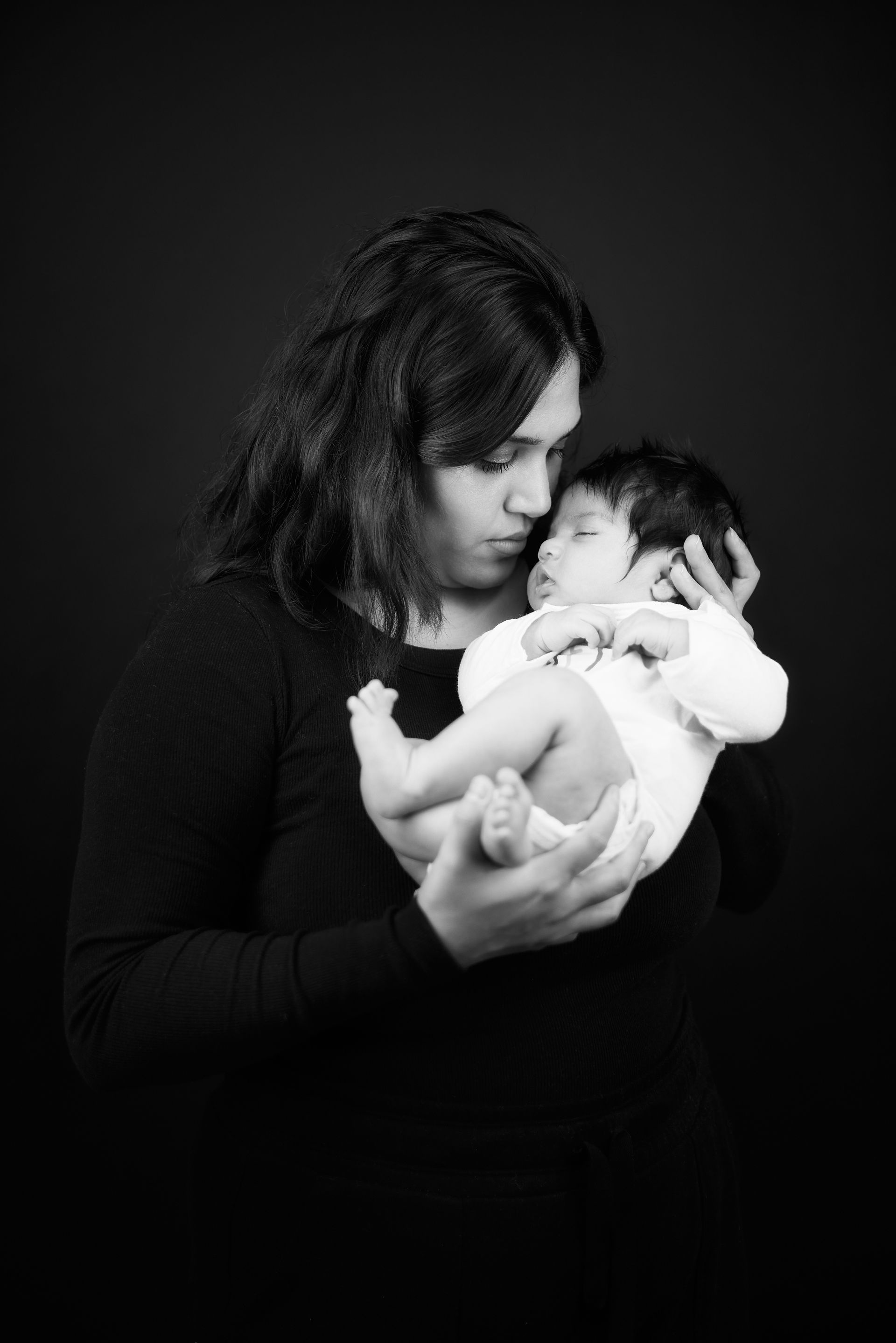 Woman holding a baby, looking down. Both are in black and white.