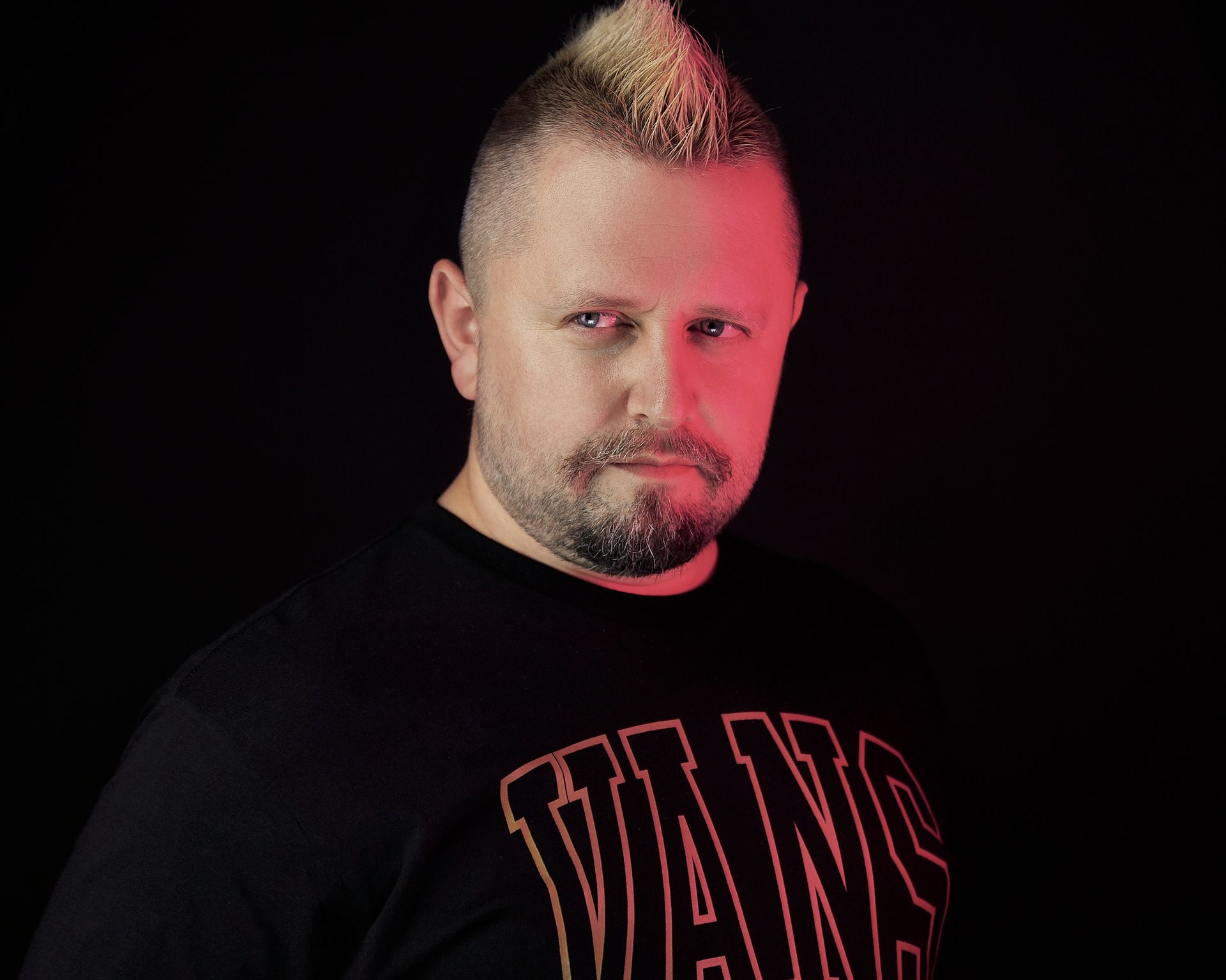 Man with a mohawk and beard, wearing a black shirt, looking at the camera.
