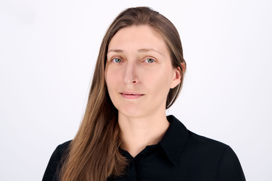 Woman with long brown hair in a black button-down shirt, looking directly at the camera.