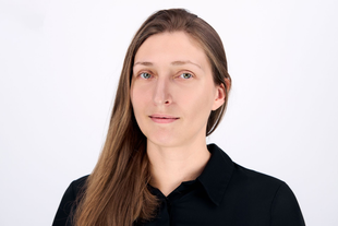 Woman with long brown hair in a black button-down shirt, looking directly at the camera.