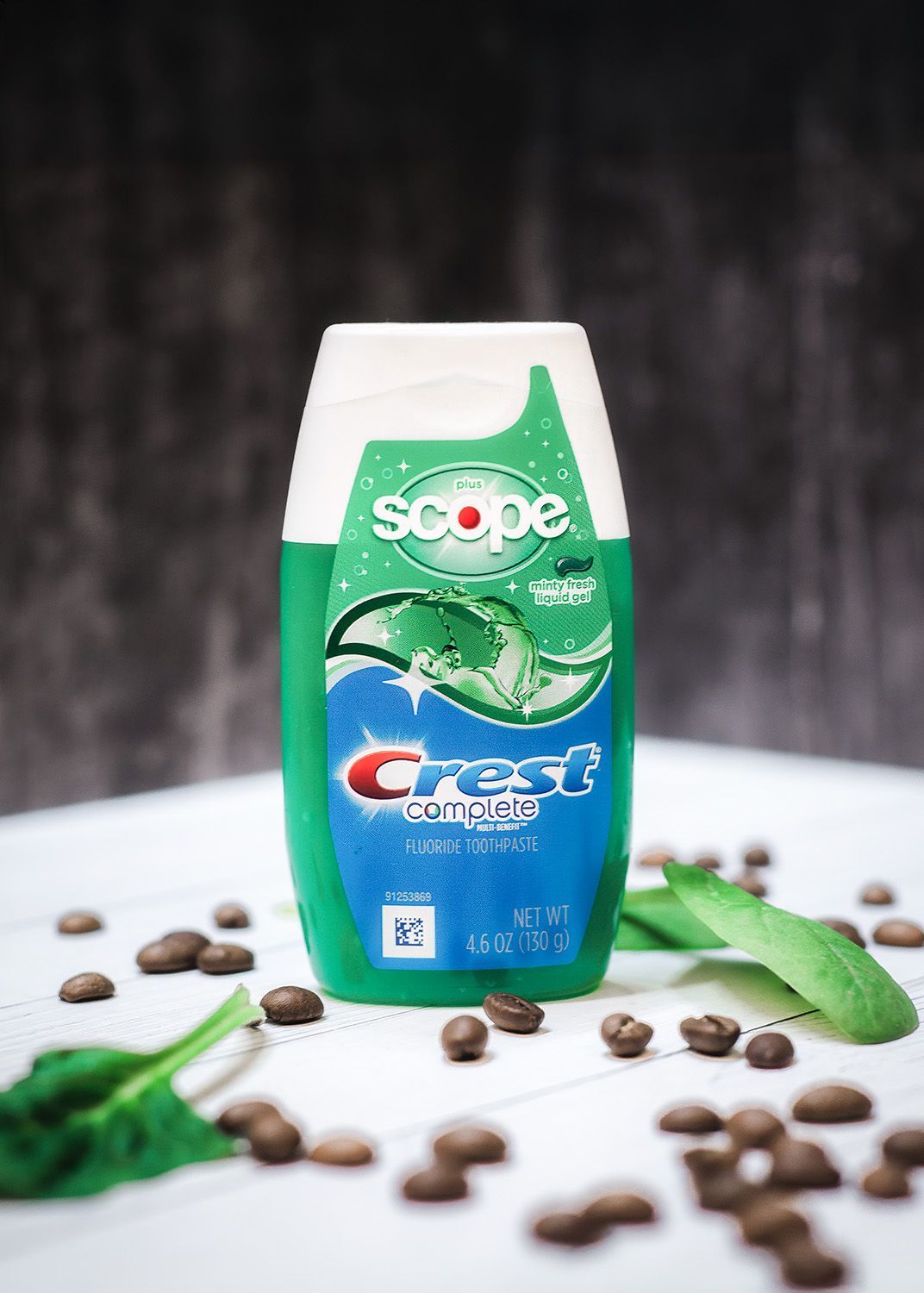 Crest mouthwash bottle with Scope, green and white label, surrounded by coffee beans and green leaves.