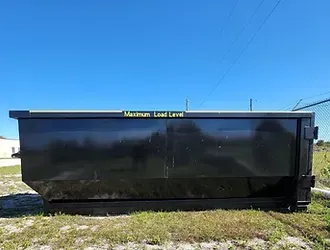 A large black dumpster is sitting in the middle of a grassy field.