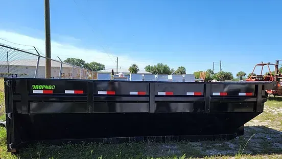 A dumpster is parked in a grassy field next to a fence.