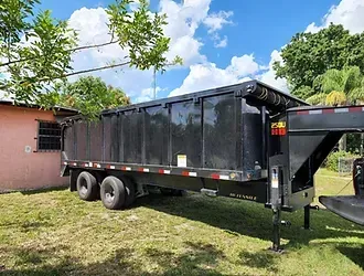 A dump trailer is parked in the grass in front of a house.