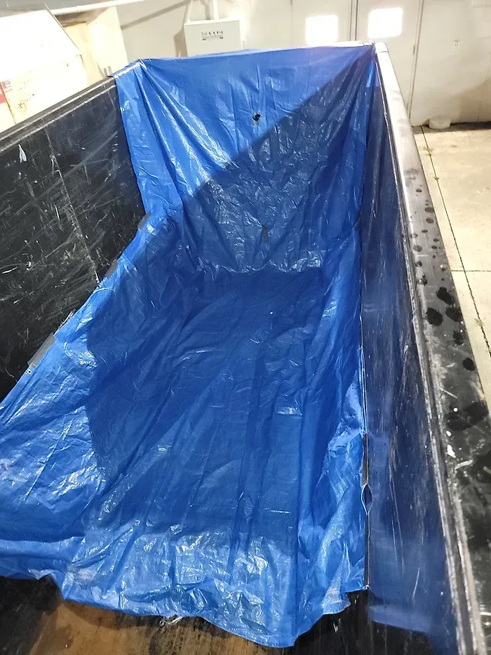 A blue tarp is covering the inside of a dumpster.