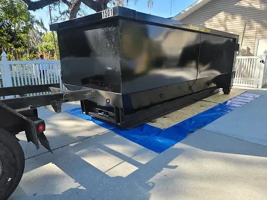 A dumpster is sitting on top of a blue tarp in a driveway.