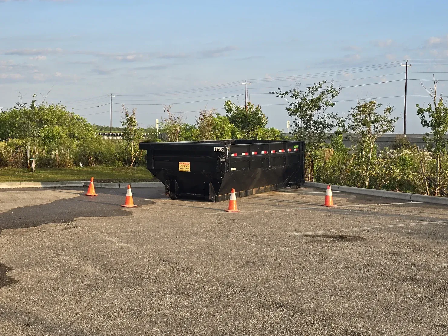 A dumpster is sitting in a parking lot next to orange cones.