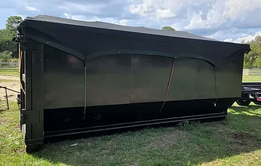 A large black dumpster is sitting on top of a lush green field.