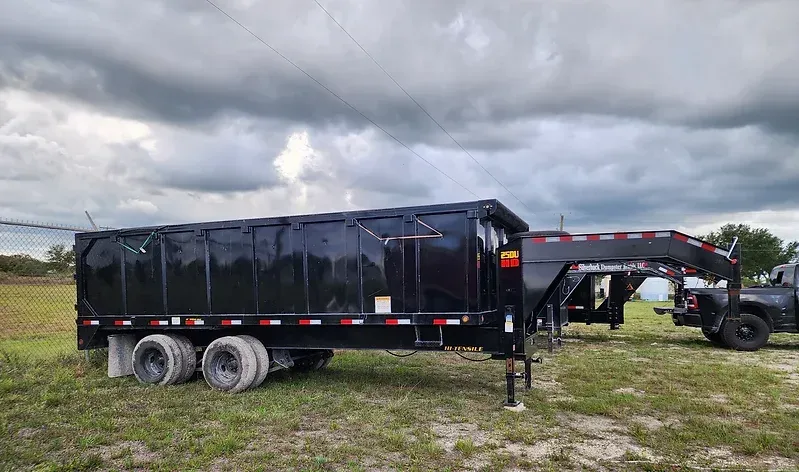 A dump trailer is parked in a grassy field next to a truck.
