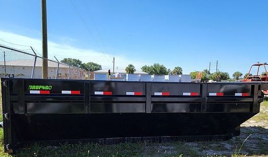 A large black dumpster is parked in a grassy field.