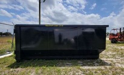 A large black dumpster is sitting in the middle of a grassy field.