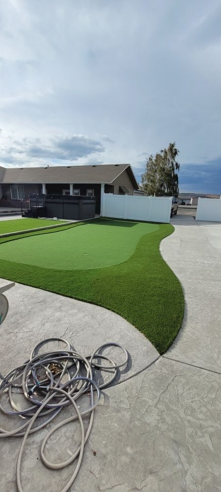 A hose is laying on the ground next to a putting green in front of a house.