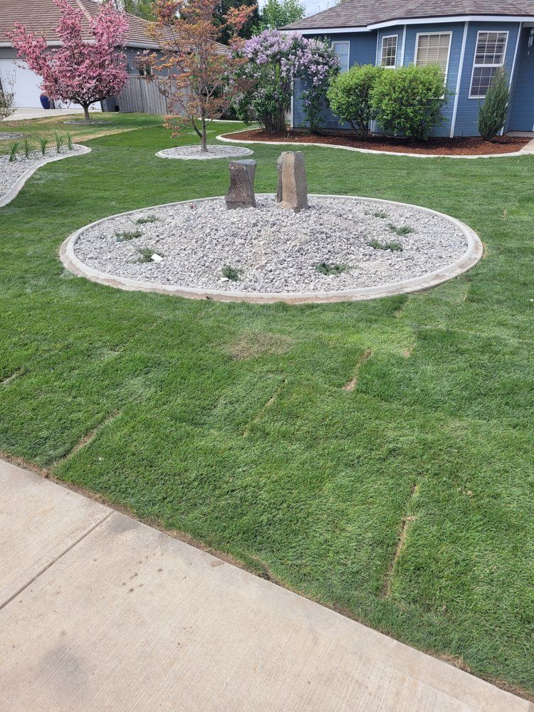 A lush green lawn with a circle of rocks in the middle of it in front of a house.