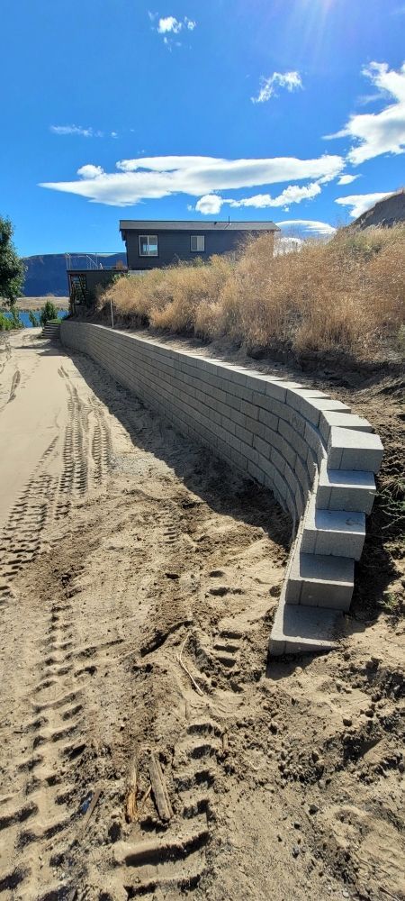 A concrete retaining wall is being built on top of a dirt hill.