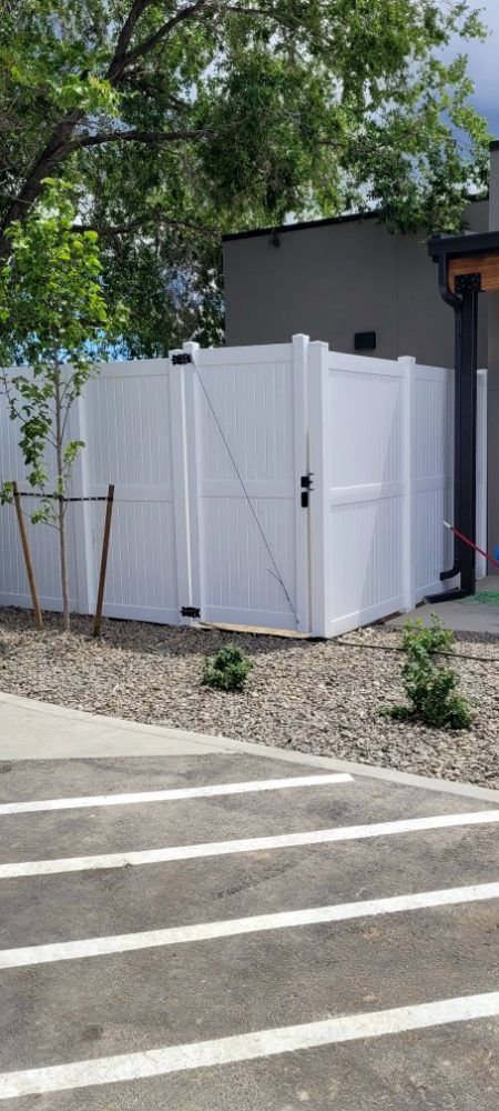 A white fence with a gate is in a parking lot next to a building.
