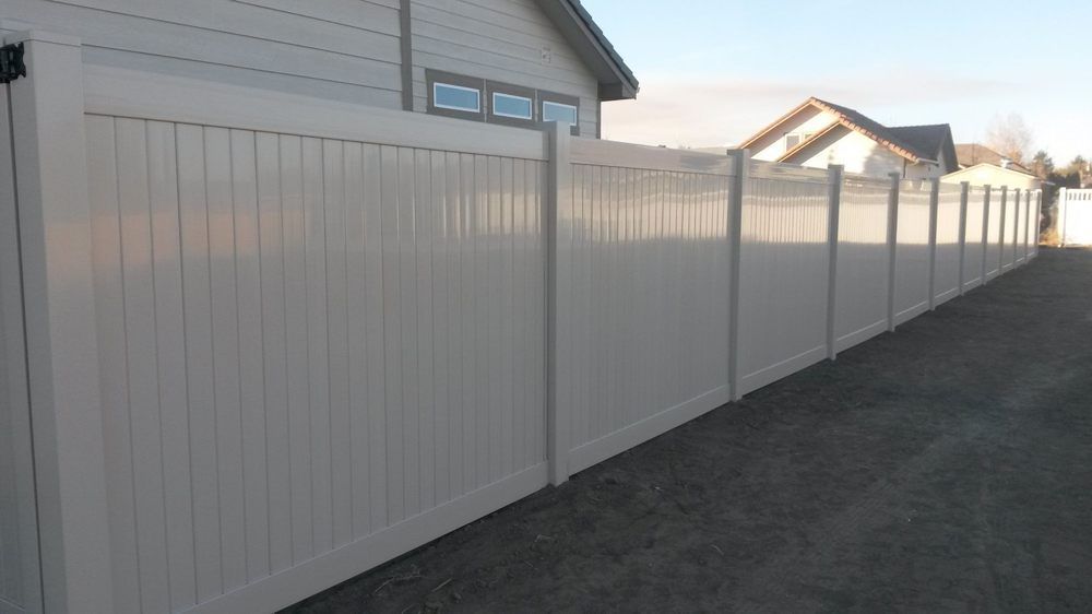 A white vinyl fence surrounds a driveway in front of a house.
