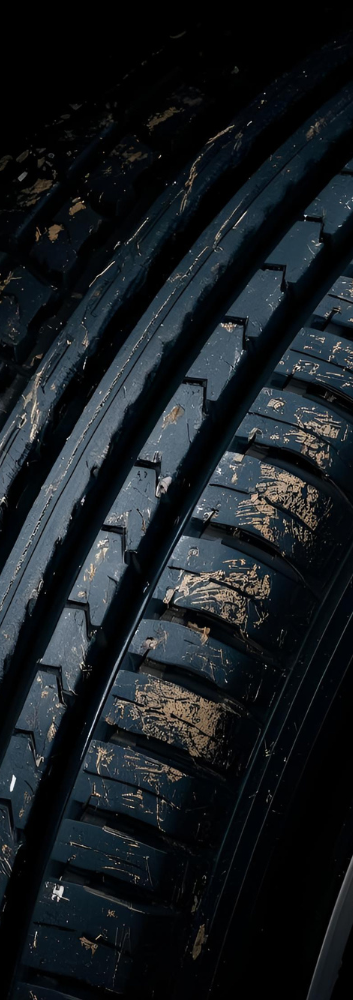 Close-up of a black tire with worn tread, covered in dirt.