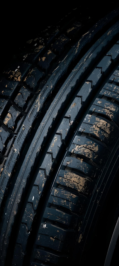 Close-up of a black tire with worn tread, covered in dirt.